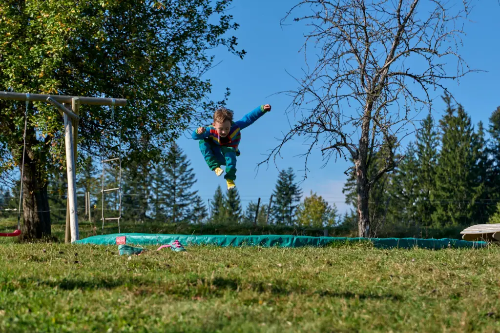 Ein Kind springt auf dem Trampolin neben der Schaukel im Garten