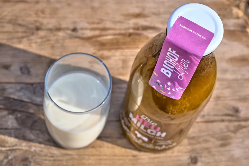 Draufsicht auf eine Bio-Heumilchflasche mit rosa Höfler-Etikett und ein Glas Milch auf Holz