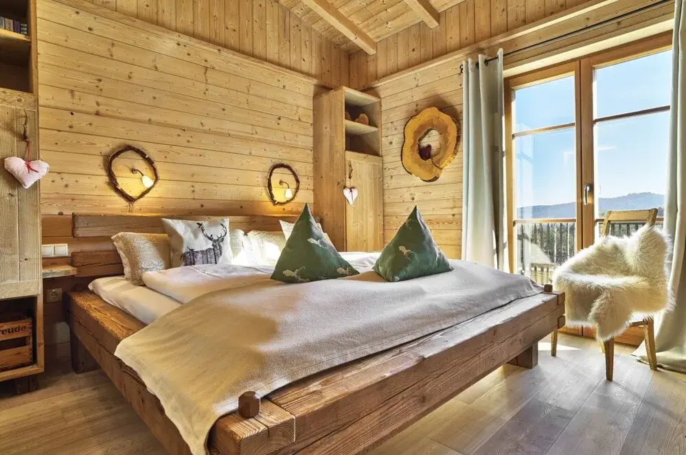 Schlafzimmer im Holzhaus mit großem Holzbett und Blick ins Freie